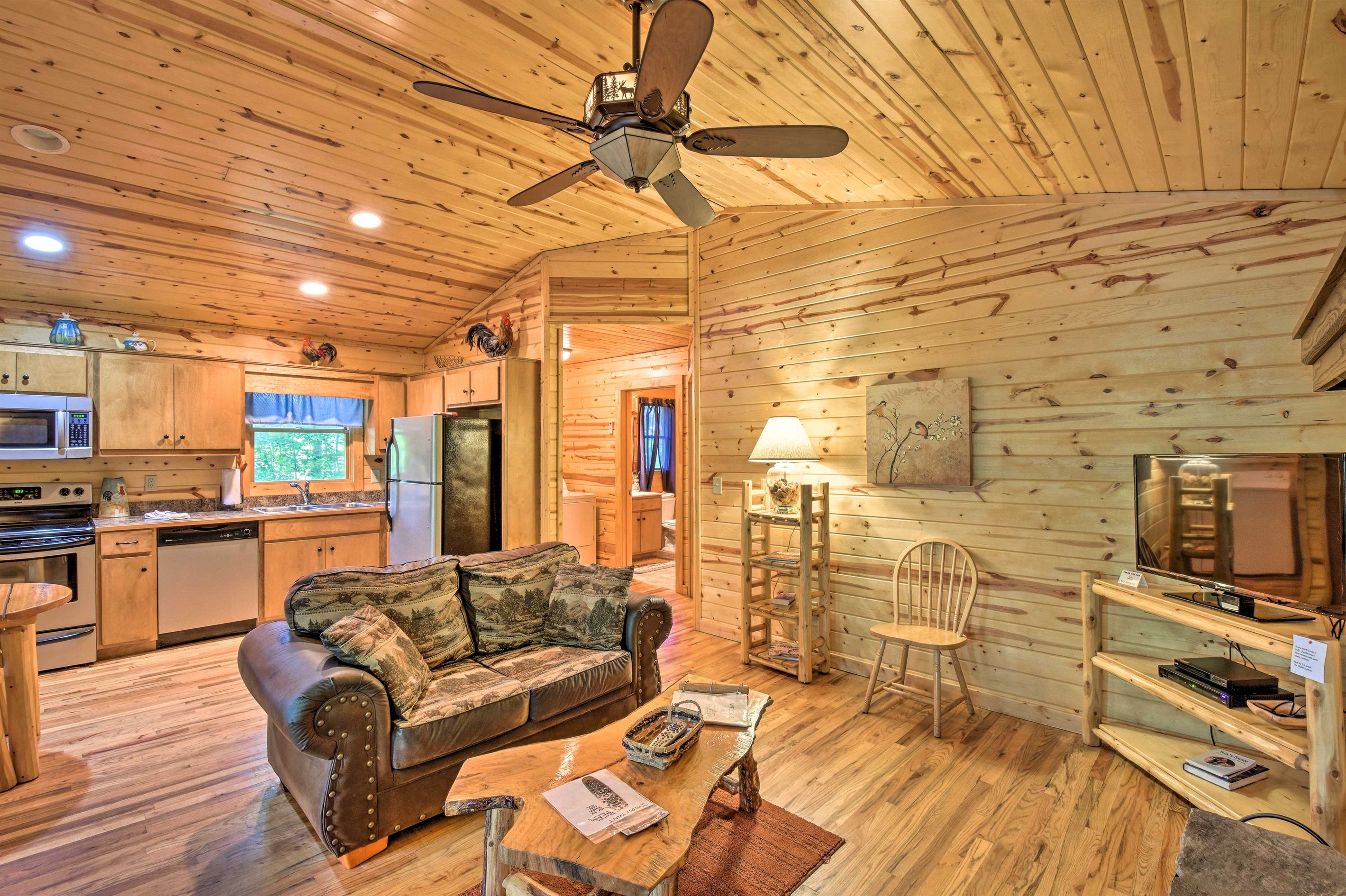 A cozy cabin interior with a wooden ceiling, a sofa, a coffee table, a TV, and a kitchen area.