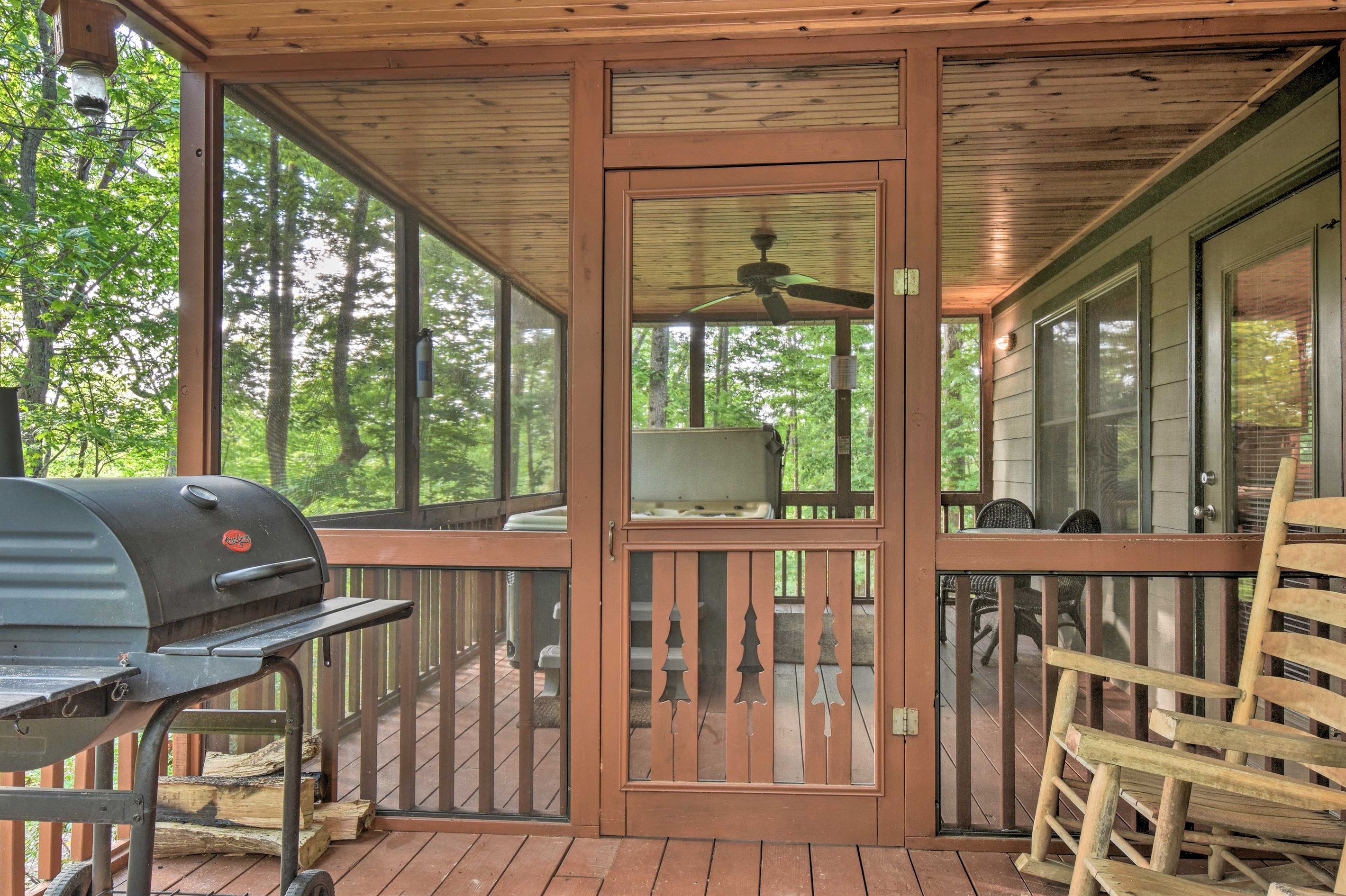 A covered porch with a grill, a rocking chair, and a view of the forest.
