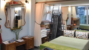 Un dormitorio con cama, ventilador de techo, cómoda, espejo, ventana con cortinas y vista a la ciudad.