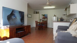 A living room with a flat-screen TV, wooden entertainment unit, dining table with chairs, a gray sofa, and a kitchen area with a refrigerator and microwave. - Bongaree Getaway, Clean Comfy, and Homely. (Bongaree)