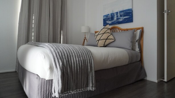 A neatly arranged bedroom with a bed, curtains, a lamp, and a painting on the wall. - Bongaree Getaway, Clean Comfy, and Homely. (Bongaree)
