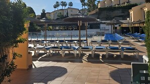A sunny outdoor area with a pool, lounge chairs, and a building with a thatched roof. - Charming 2-bedroom chalet with AC, WiFi in wonderful Málaga (AN)