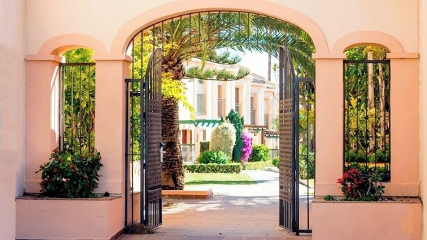 An arched entrance to a building with a garden view, featuring a palm tree and a well-maintained lawn. - Charming 2-bedroom chalet with AC, WiFi in wonderful Málaga (AN)