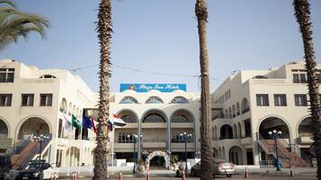A hotel with a central archway, palm trees, and a sign reading "Plaza Inn Hotels".