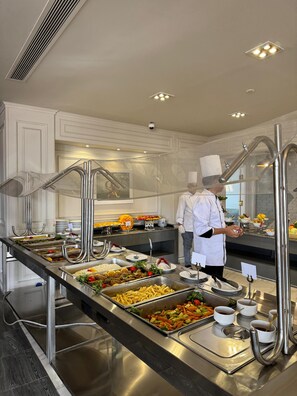 A buffet setup with multiple food stations, a chef, and a security camera on the ceiling. - oriental grand plaza (Tenth of Ramadan City)