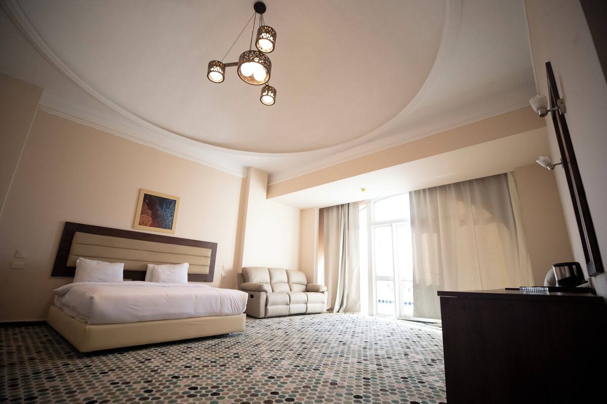 A hotel room with a bed, a sofa, a desk, and a chandelier.