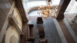 A spacious lobby with a grand chandelier, a seating area with sofas and armchairs, and a large arched window. - oriental grand plaza (Tenth of Ramadan City)
