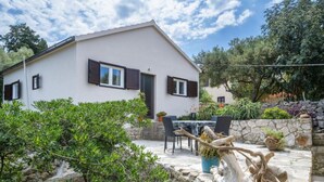 A white building with dark shutters, a stone wall, and a patio with outdoor furniture. - Holiday Home Seafront Oleandar (Blato)