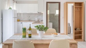 A modern kitchen with white cabinets, a wooden dining table, and a potted plant. - Holiday Home Seafront Oleandar (Blato)