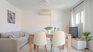 A modern living room with a sofa, two chairs, a dining table, a TV, and a potted plant. - Holiday Home Seafront Oleandar (Blato)