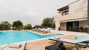 A modern outdoor pool area with lounge chairs and a table, surrounded by a stone building with a balcony. - Villa Felicity B4 (Sibenik)