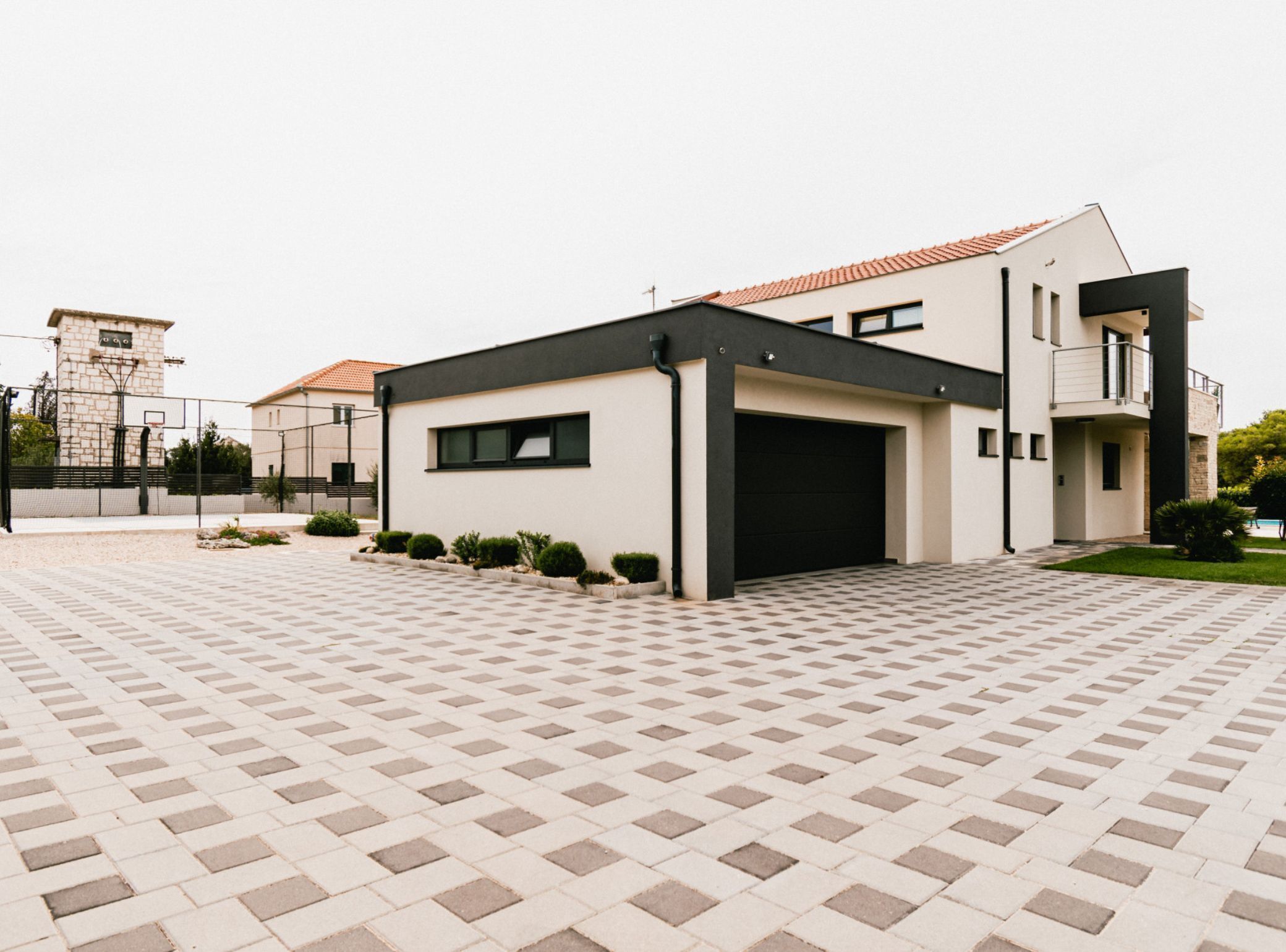 A modern two-story house with a black garage door, a small balcony, and a paved driveway.