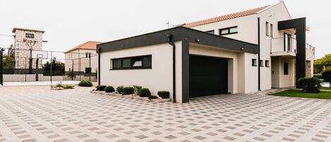 A modern two-story house with a black garage door, a small balcony, and a paved driveway.
