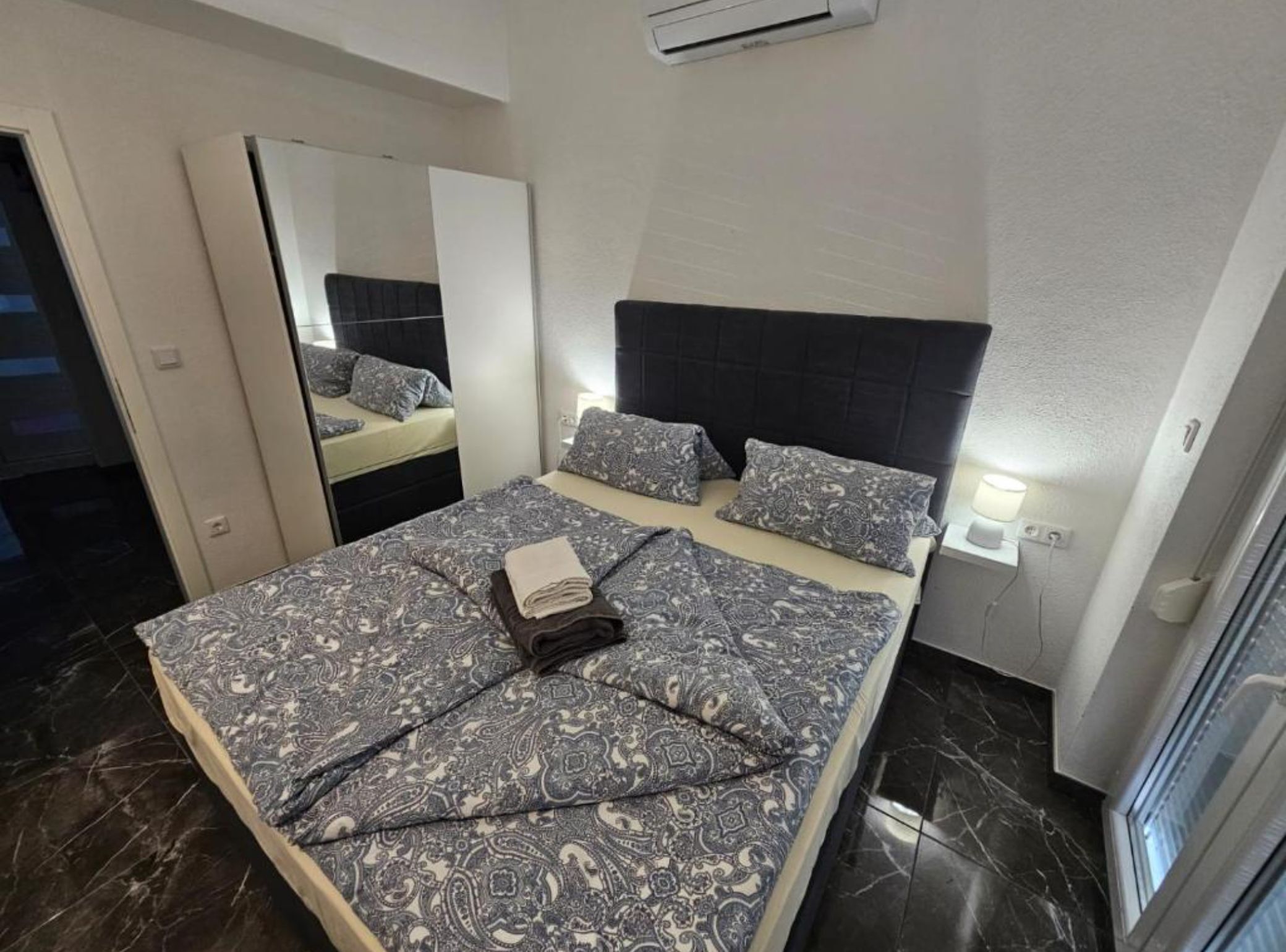 Ein modernes Schlafzimmer mit einem großen Bett, einem Spiegel und einer Wandklimaanlage.