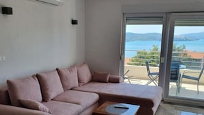 A modern living room with a pink sectional sofa, a small wooden table, and a large sliding glass door leading to a balcony with a view of the sea and hills. - Spacious Villa With Outdoor Swimming Pool in Trogir (Okrug)
