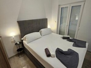 Ett hotellrum med en säng, ett litet sängbord, en stol och ett fönster med persienner.