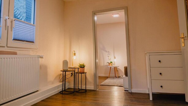 A hallway with a radiator, a small table with a plant, a white dresser, and a door leading to another room. - Apartment in Vallendar Near Rhine Promenade (Vallendar)