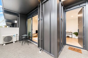 Une façade moderne avec une entrée dotée d’une porte-fenêtre coulissante, un petit espace patio avec une table et des chaises, et un paillasson.