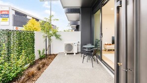 Une terrasse extérieure moderne, dotée d’un espace salon, d’un appareil de climatisation et d’une porte vitrée donnant sur un espace intérieur.
