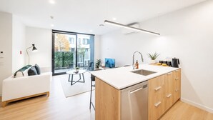 Une cuisine moderne dotée d’un grand îlot central, de meubles en bois et d’un lave-vaisselle. On y trouve également un coin repas avec une table et des chaises, ainsi qu’un canapé.