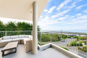 Un balcon avec un canapé blanc, un banc en bois et une vue sur une route et la verdure.