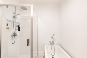 Een moderne badkamer met een douchecabine van glas, een vrijstaand bad en een klein plankje met toiletartikelen.