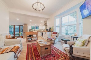 Un salón espacioso con un sofá, un sillón y una mesa de centro de madera. Se aprecia una cocina con una mesa de comedor y sillas al fondo.