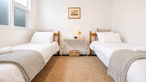 Une chambre avec deux lits simples, une petite table avec une lampe, un tableau encadré au mur et un tapis tissé sur le sol.