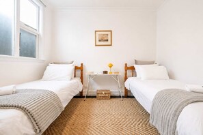 A room with two single beds, a small table with a lamp, a framed picture on the wall, and a woven rug on the floor. - Stylish Central Cottage | Modern Heating & Parking (Christchurch)