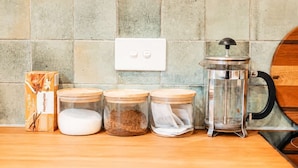 Un comptoir de cuisine avec une boîte de thé chai, trois bocaux en verre avec des couvercles et une cafetière à piston.