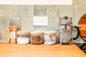 A kitchen counter with a box of chai tea, three glass jars with lids, and a French press. - Stylish Central Cottage | Modern Heating & Parking (Christchurch)