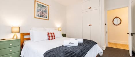 A neatly arranged bedroom with a bed, bedside tables, a wardrobe, and a door leading to another room.
