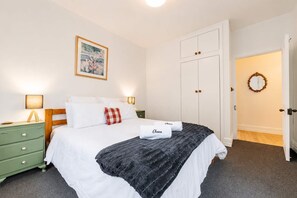 Een keurig opgemaakt slaapkamer met een bed, nachtkastjes, een kledingkast en een deur naar een andere kamer.
