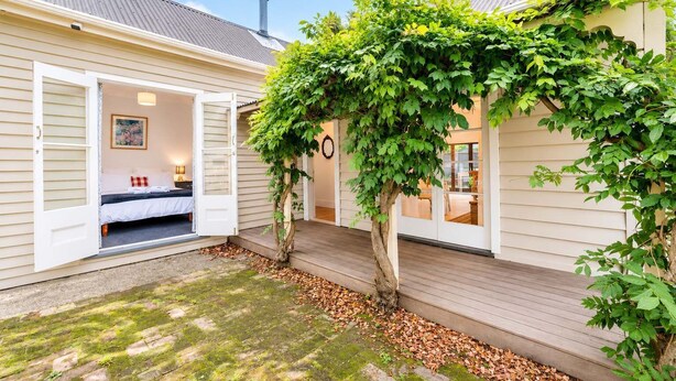 Un charmant chalet doté d’une terrasse en bois, d’un lit avec une tête de lit blanche et d’un grand arbre qui offre de l’ombre.