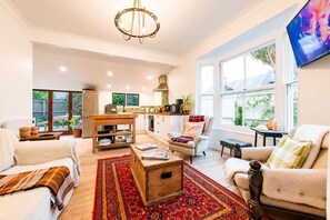 A spacious living room with a large window, a dining area, and a kitchen. - Stylish Central Cottage | Modern Heating & Parking (Christchurch)