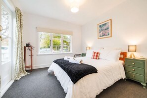 Een slaapkamer met een bed, nachtkastjes, een raam en een schilderij aan de muur.