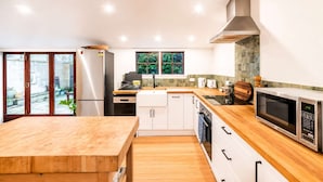 Une cuisine moderne dotée d’un plan de travail en bois, d’appareils électroménagers en acier inoxydable et d’une porte-fenêtre coulissante donnant sur un jardin.