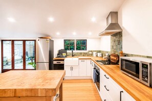 A modern kitchen with a wooden countertop, stainless steel appliances, and a sliding glass door leading to a garden. - Stylish Central Cottage | Modern Heating & Parking (Christchurch)