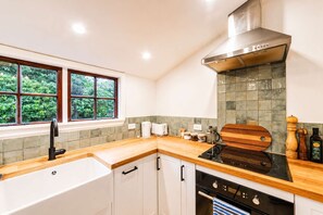 A modern kitchen with a wooden countertop, stainless steel appliances, and a window with a view of greenery.