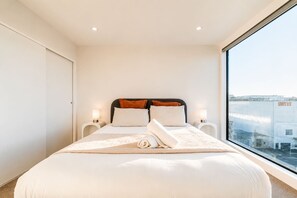 A hotel room with a large bed, two bedside tables, and a view of the city through a large window.