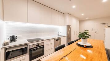 Una cocina moderna con armarios blancos, un refrigerador de acero inoxidable, horno empotrado y una mesa de comedor de madera con una planta en maceta.