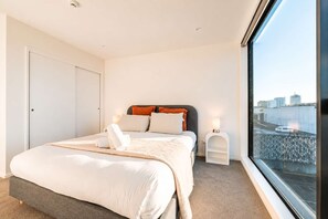 Een moderne hotelkamer met een groot bed, een nachtkastje, een raam met uitzicht op de stad, en een deur.