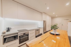 Une cuisine moderne avec des meubles blancs, des appareils en acier inoxydable et une table à manger en bois agrémentée d’une plante en pot.
