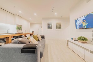 A modern living room with a grey sofa, wooden coffee table, and a flat-screen TV mounted on the wall.