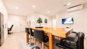 A modern kitchen with a wooden table and chairs, a built-in oven, and a flat-screen TV mounted on the wall.