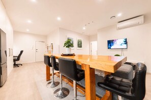A modern kitchen with a wooden table and chairs, a built-in oven, and a flat-screen TV mounted on the wall.