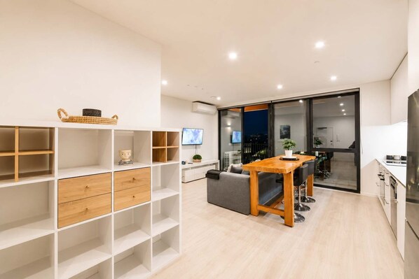 A modern living space with a dining area, kitchen, and a large window overlooking a cityscape.