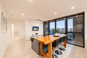 Un interior moderno con una mesa de comedor de madera, sillas negras, un televisor en la pared y un balcón con vistas a la ciudad.