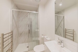 A modern bathroom with a glass shower enclosure, a white toilet, and a sink with a mirror.