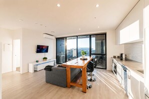 A modern apartment with a dining area, kitchenette, and a large window offering a city view.